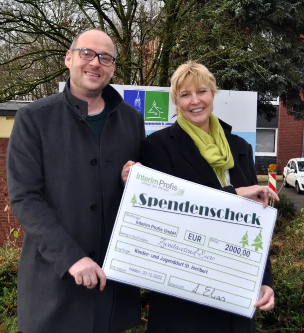 Fotografie der Spendenübergabe mittels großen Check mit Annette Elias, Inhaberin der Interim Profis und Ansprechpartner des Jugend- und Kinderdorf St. Heribert 