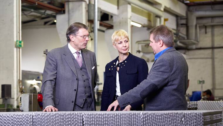 Interim Management für den Mittelstand Zwei Manager und Geschaeftsfuehrerin Annette Elias stehen in einer Produktionshalle und sprechen miteinander
