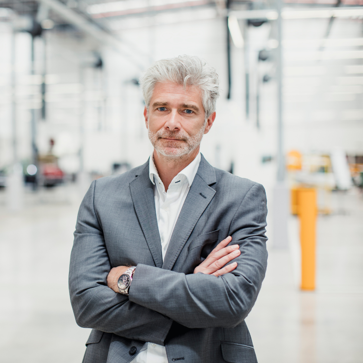 Ein Portrait von einem Senior Manager, der mit verschraenkten Armen in einer Produktionshalle steht.