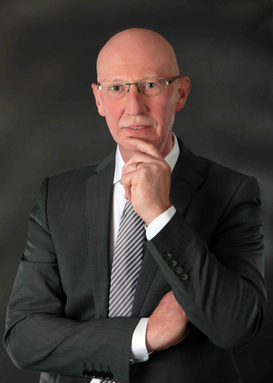 Interim CRO Restrukturierungsmanager Ein Interim Manager steht in einer Produktionshalle mit Anzug und hat eine Hand auf einem Tisch abgelegt