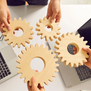 Zwei Personen halten Zahnräder aus Holz in den Händen - es steht symbolisch für Zusammenhänge