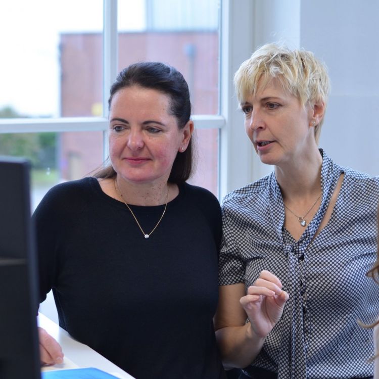 Interim Management für den Mittelstand Claudia Kohlmann Consultant bei den Interim Profis und Annette Elias Geschäftsführerin der Interim Profis stehen an einem Schreibtisch in einem Buero mit Fenster