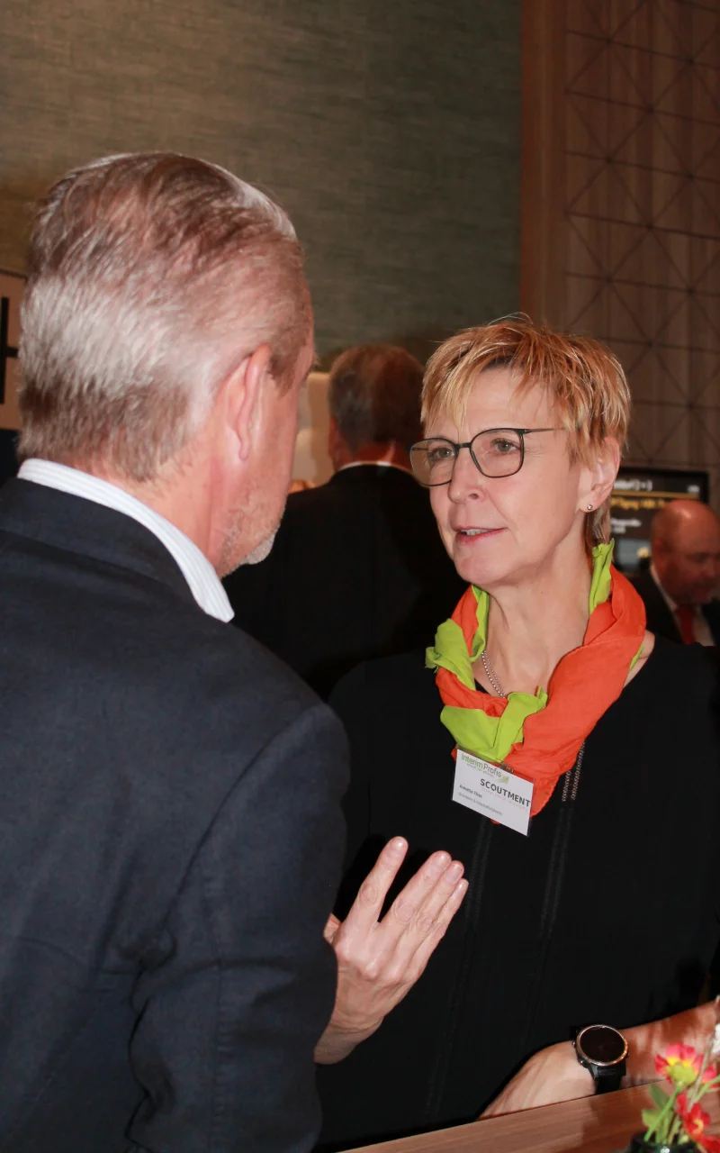 Interim Management für den Mittelstand Annette Elias steht mit einem Interim Manager an einem Hochtisch und ist in einem Gespraech